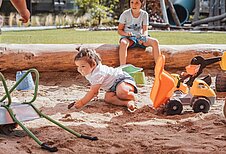 Kind spielt im Sandkasten auf dem Outdoor-Spielplatz des Familienhotels Huber in Südtirol