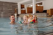 Eine glückliche Familie die im Indoor-Pool plantscht. 