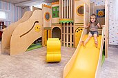 Ein Mädchen rutsch eine kleine Rutsche auf einem kleinen Indoor-Spielplatz im Familienhotel Rhön Feeling