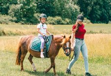 Ein Mädchen reitet fröhlich auf einem Pony über die Wiese des Familienhotel Friedrichshof.