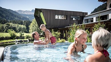 Familie planscht im Outdoor-Pool des Alphotel Tyrol Wellness & Family Resort in Südtirol.