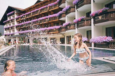 Zwei Mädchen planschen voller Freude im Außenpool des Familienhotels Kirchheimerhof in Kärnten.