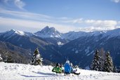 Familie beim Schlittenfahren auf dem Außengelände des Familienhotels Huber.