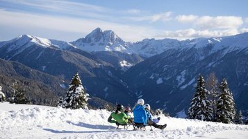 Familie beim Schlittenfahren auf dem Außengelände des Familienhotels Huber.