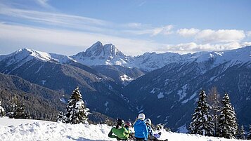 Familie beim Schlittenfahren auf dem Außengelände des Familienhotels Huber.