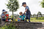 Drei Kleinkinder spielen fröhlich im Sandkasten des Familienhotels Landhuus Laurenz im Münsterland.