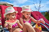 Zwei Mädchen sitzen im Liegestuhl und essen eine Wassermelone im Familienhotel Amiamo im Salzburger Land