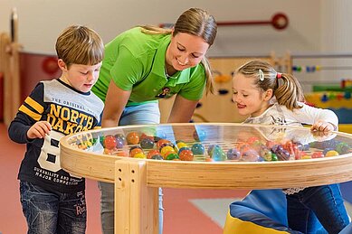 Eine Kinderbetreuerin spielt ein Bällespiel mit zwei Kindern im Familienhotel Zauchenseehof im Salzburger Land