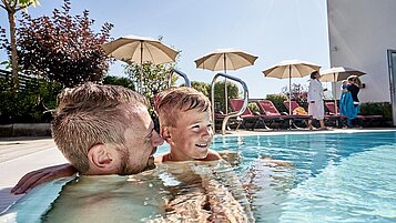 Vater und Sohn planschen glücklich im Außenpool des Familienhotels Amiamo im Salzburger Land.