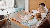 Dreiköpfige Familie entspannt im Bademantel im Familien-Wellnessbereich im Habachklause Familien Bauernhof Resort im Salzburger Land.