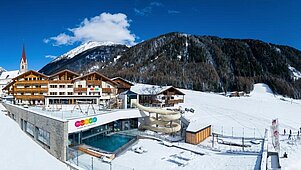 Das Familienhotel Huber in Südtirol umgeben von einer winterlichen Berglandschaft und großzügigen Außenanlage mit viel Platz zum Spielen für Kinder.