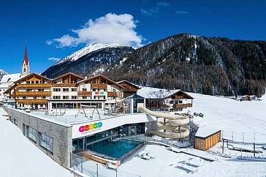 Das Familienhotel Huber in Südtirol umgeben von einer winterlichen Berglandschaft und großzügigen Außenanlage mit viel Platz zum Spielen für Kinder.