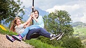 Zwei Maedchen schingen durch den Spielplatz auf dem Schwingeil im Kinderhotel Sailer in Tirol.