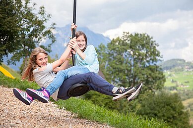 Zwei Maedchen schingen durch den Spielplatz auf dem Schwingeil im Kinderhotel Sailer in Tirol.