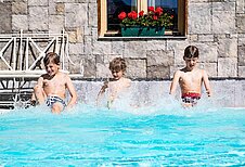 3 Kinder sitzen am Beckenrand vom Pool und planschen mit den Beinen im Basser vom Familienhotel Hotel Tirolerhof an der Zugspitze.