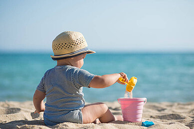 Baby spielt mit Sand am Strand an der Ostsee.