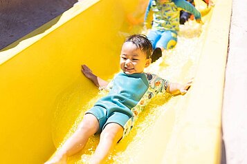 Kleiner Junge rutscht mit großer Freude eine gelbe Wasserrutsche im Familienhotel Landhaus zur Ohe im Bayerischen Wald hinunter.