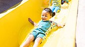 Kleiner Junge rutscht mit großer Freude eine gelbe Wasserrutsche im Familienhotel Landhaus zur Ohe im Bayerischen Wald hinunter.