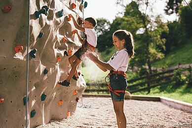 Ein Mädchen steht vor dem Kletterfels im Outoorgelände vom Familienhotel Post Family Resort im Salzburger Land.