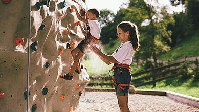 Ein Mädchen steht vor dem Kletterfels im Outoorgelände vom Familienhotel Post Family Resort im Salzburger Land.