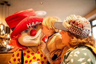 Das Familotel Maskottchen Happy sitzt im Restaurant am Tisch einer Familie im Familienhotel Landhaus zur Ohe im Bayerischen Wald.