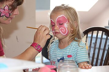 Ein Mädchen wird von einer Kinderbetreuerin im Gesicht geschminkt