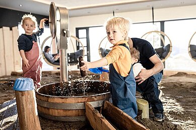 Zwei Kinder spielen in Matschhose im Sandkasten mit einem Wasserspiel im Familienhotel Allgäuer Berghof im Allgäu.