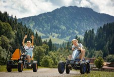 Zwei Kinder fahren lachend mit Gokarts über das Gelände des Familienhotels Krone im Allgäu, im Hintergrund die Berge.
