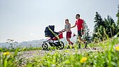 Eltern gehen mit einem Kinderwagen spazieren im Familienurlaub im Allgäuer Berghof.