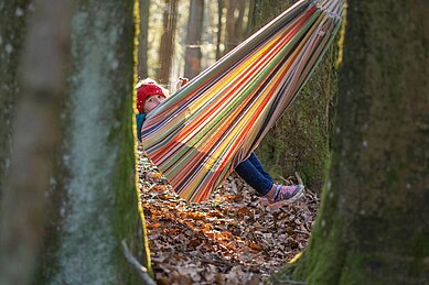 Kind sitzt in einer Hängematte im Waldkinder Club im Familienhotel Landhaus zur Ohe.