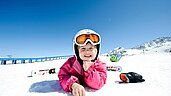 Kleinkind sitzt auf einer Schaukel auf dem Outdoor-Spielplatz des Familienhotels Alpenhotel Kindl in Tirol.