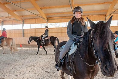 Mädchen sitzt auf einem Pferd und reitet in der Reithalle des Familienhotels Landhaus zur Ohe.