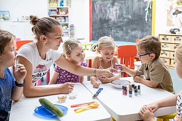 Lachende Kinder gemeinsam mit einer Betreuerin in der Kinderbetreuung im Familienhotel Kaiserhof in Tirol.