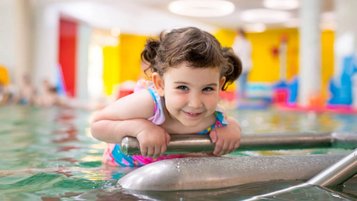 Strahlender Badespaß im Familienhotel Ungarn: Ein fröhliches Mädchen genießt das warme Wasser im Kinderpool des Kolping Family Resort.