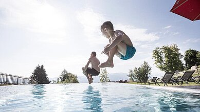 Zwei Kinder springen in den Pool im Familienhotel Allgäuer Berghof.