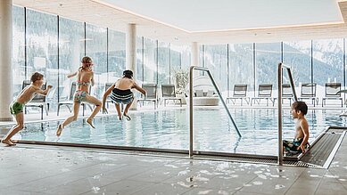 Drei Kinder springen in den Indoorpool im Almfamilyhotel Scherer in Tirol