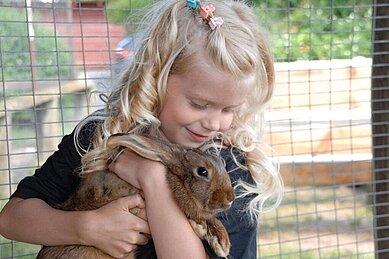 Mädchen kuschelt mit einem Hasen im Kleintierbereich des Bernsteinreiter Schlossresorts