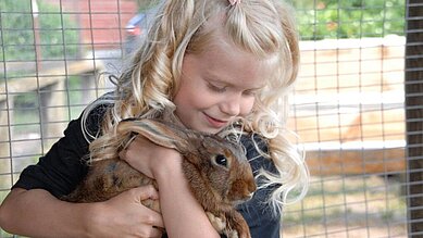 Mädchen kuschelt mit einem Hasen im Kleintierbereich des Bernsteinreiter Schlossresorts