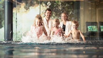 Familie planscht am Beckenrand im Indoor-Pool des Familienhotel