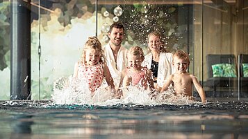 Familie planscht am Beckenrand im Indoor-Pool des Familienhotel