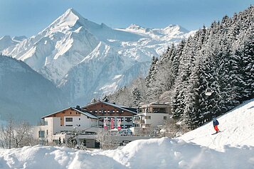 Blick auf das Familienhotel Amiamo im Winter, im Hintergrund ein schneebedeckter Berg 