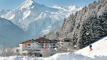 Blick auf das Familienhotel Amiamo im Winter, im Hintergrund ein schneebedeckter Berg 