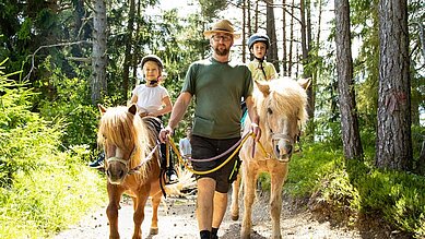 Zwei Kinder bei einem geführten Ponyausritt im Wald im Familienhotel Lärchenhof in Tirol