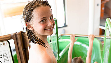 Familienhotel Wasserspaß: Teenie steht oben an der Wasserrutsche und grinst in die Kamera
