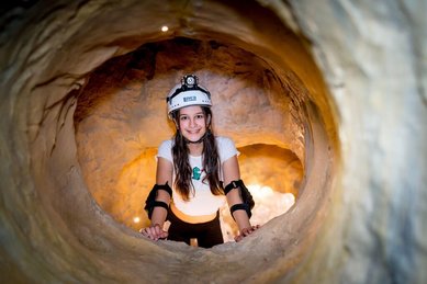 Höhlenabenteuer im Familienhotel Ungarn: Ein Mädchen erkundet strahlend den Klettertunnel im Kolping Family Resort – ein spannendes Erlebnis für kleine Entdecker.