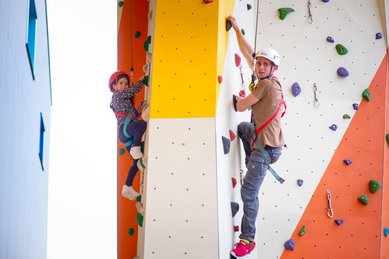 Kletterspaß für die ganze Familie: Ein Vater und sein Kind erklimmen gemeinsam die bunte Kletterwand im Kolping Family Resort in Ungarn – dem perfekten Familienhotel für aktive Urlauber.