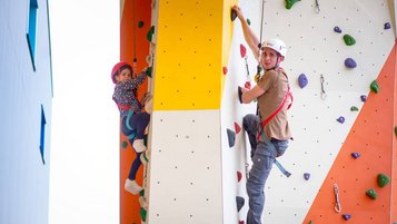 Kletterspaß für die ganze Familie: Ein Vater und sein Kind erklimmen gemeinsam die bunte Kletterwand im Kolping Family Resort in Ungarn – dem perfekten Familienhotel für aktive Urlauber.