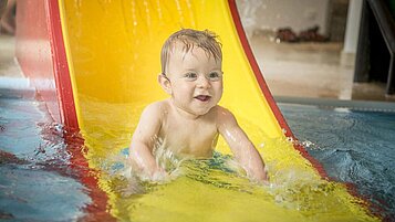 Baby auf der Babyrutsche im Kinderplanschbecken des Familienhotels Landgut Furtherwirt.