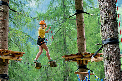 Mädchen klettert im Hochseilgarten in Tirol.