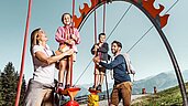 Eltern spielen mit ihren beiden Kindern auf dem Außenspielplatz des Familienhotels Amiamo im Salzburger Land.